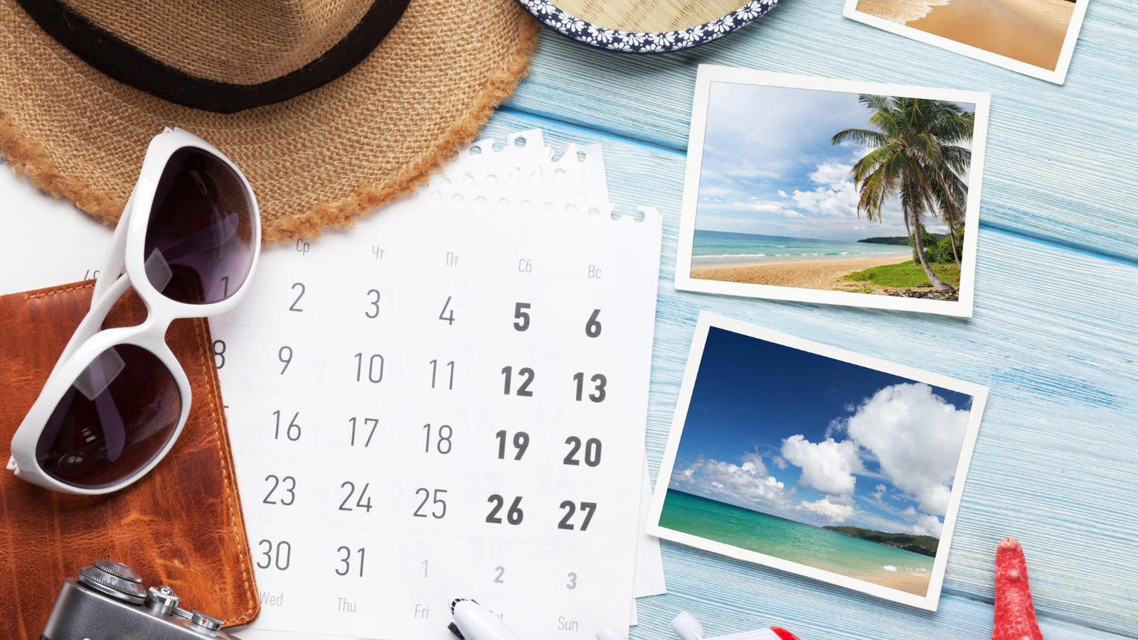 Kalender zur Urlaubsplanung mit Sonnenhut, Sonnenbrille und Strandfotos auf einem Holztisch